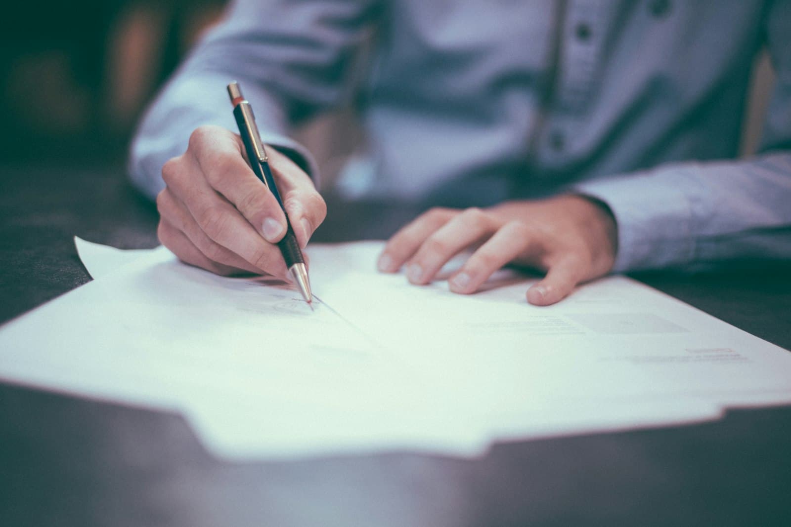Primo piano di una mano che firma un foglio con una penna, appoggiata su un tavolo