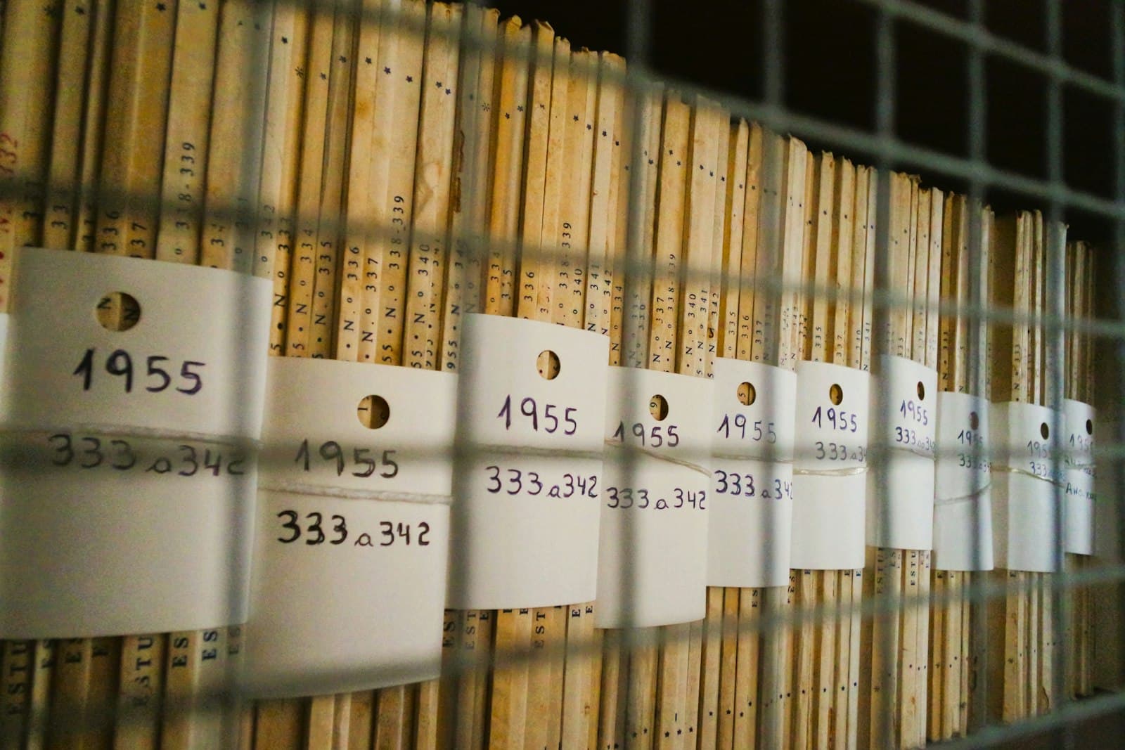 Scaffale d'archivio con file di cartelle d'epoca, ciascuna con un cartellino che riporta l'anno 1955