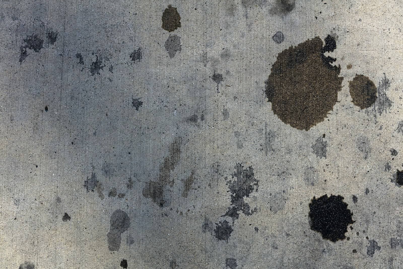 Macchie scure d'olio su una pavimentazione chiara di cemento
